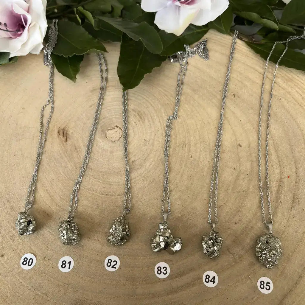 Pendentif Pyrite Brute en plusieurs styles, suspendu sur des chaînes argentées avec des fleurs en arrière-plan