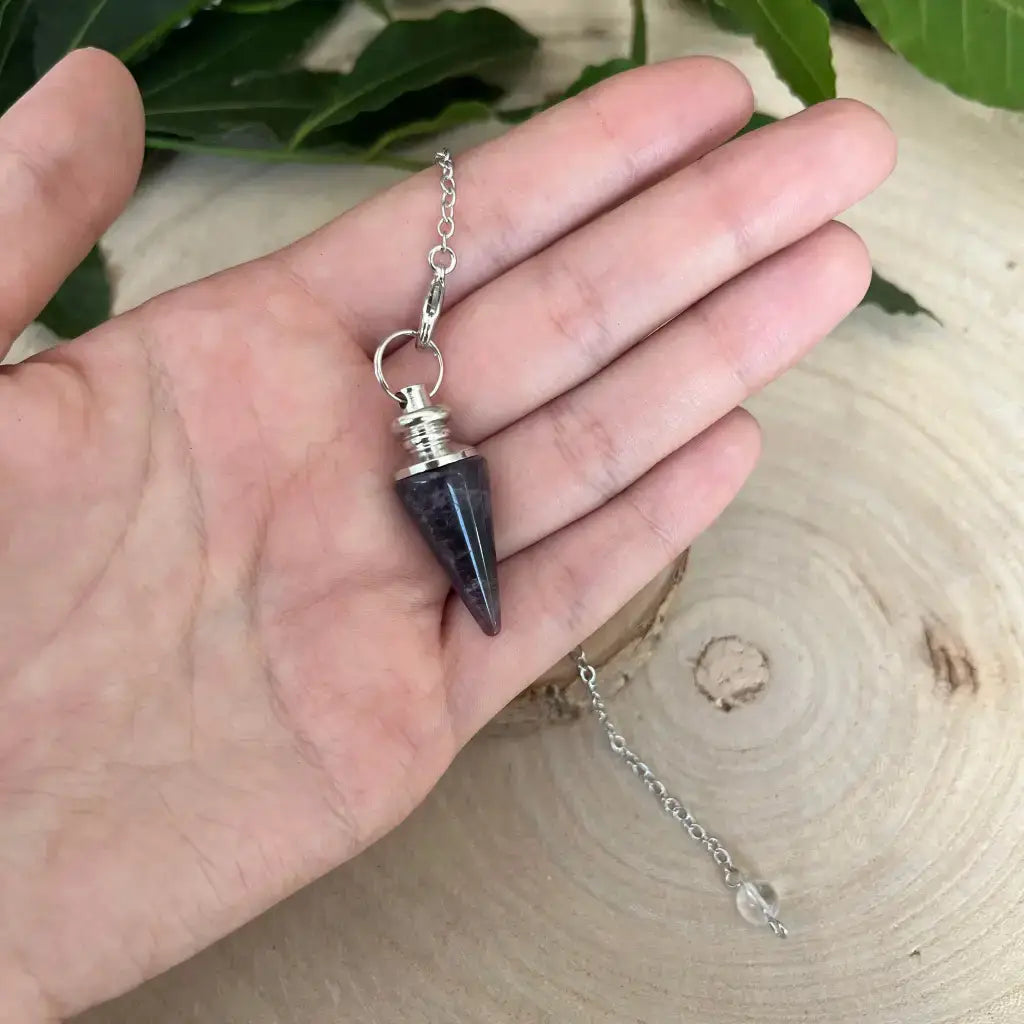 Pendule en Améthyste Aura de Roche petit pendule conique en pierre violette avec chaîne argentée tenu à la main