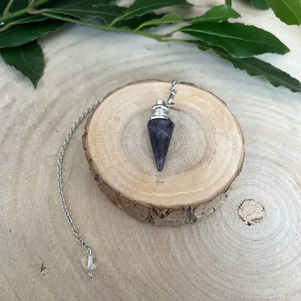 Pendule en Améthyste conique monté sur chaîne argentée posé sur tranche de bois naturel