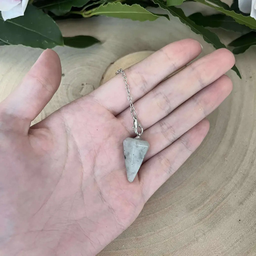 Pendule en Labradorite à pointe facettée sur chaîne argentée tenu dans la paume pour radiesthésie