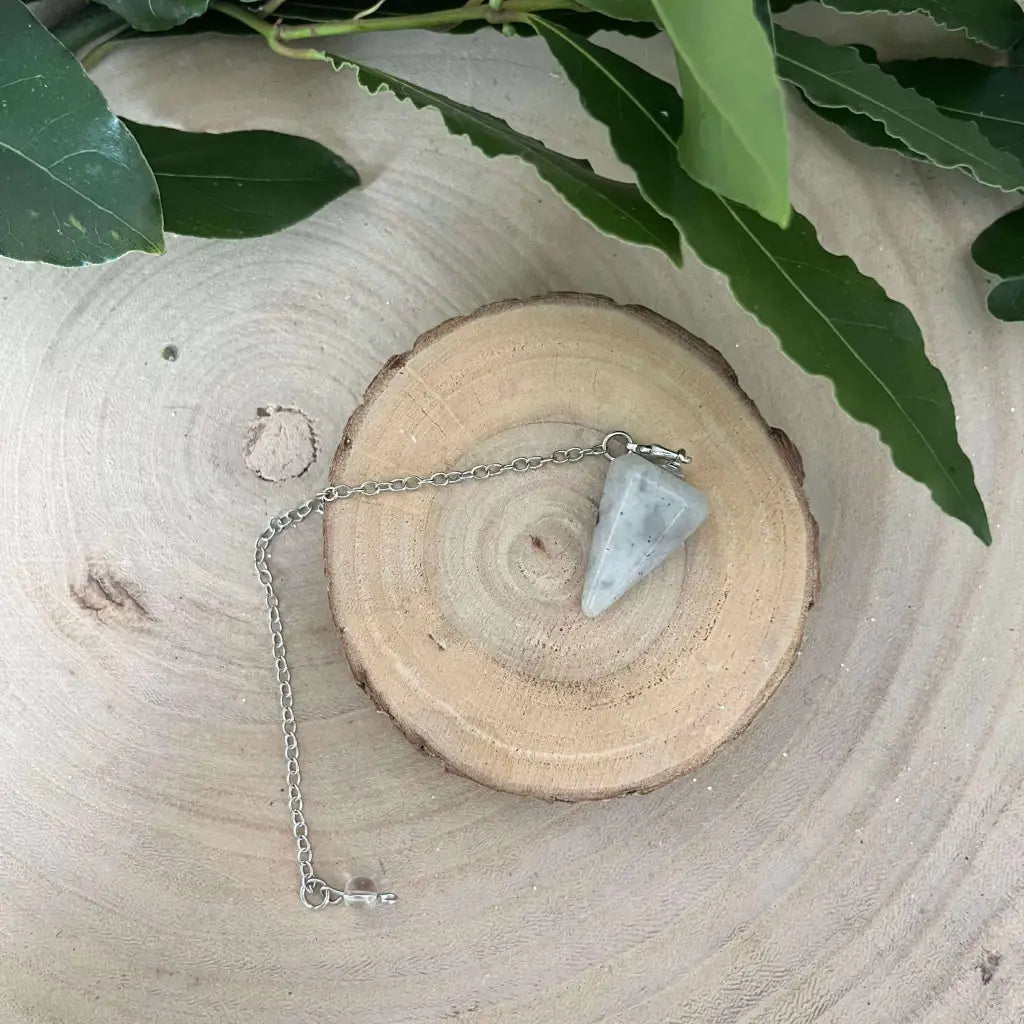 Pendule en Labradorite Aura de Roche posé sur tranche de bois avec chaîne métallique pour radiesthésie
