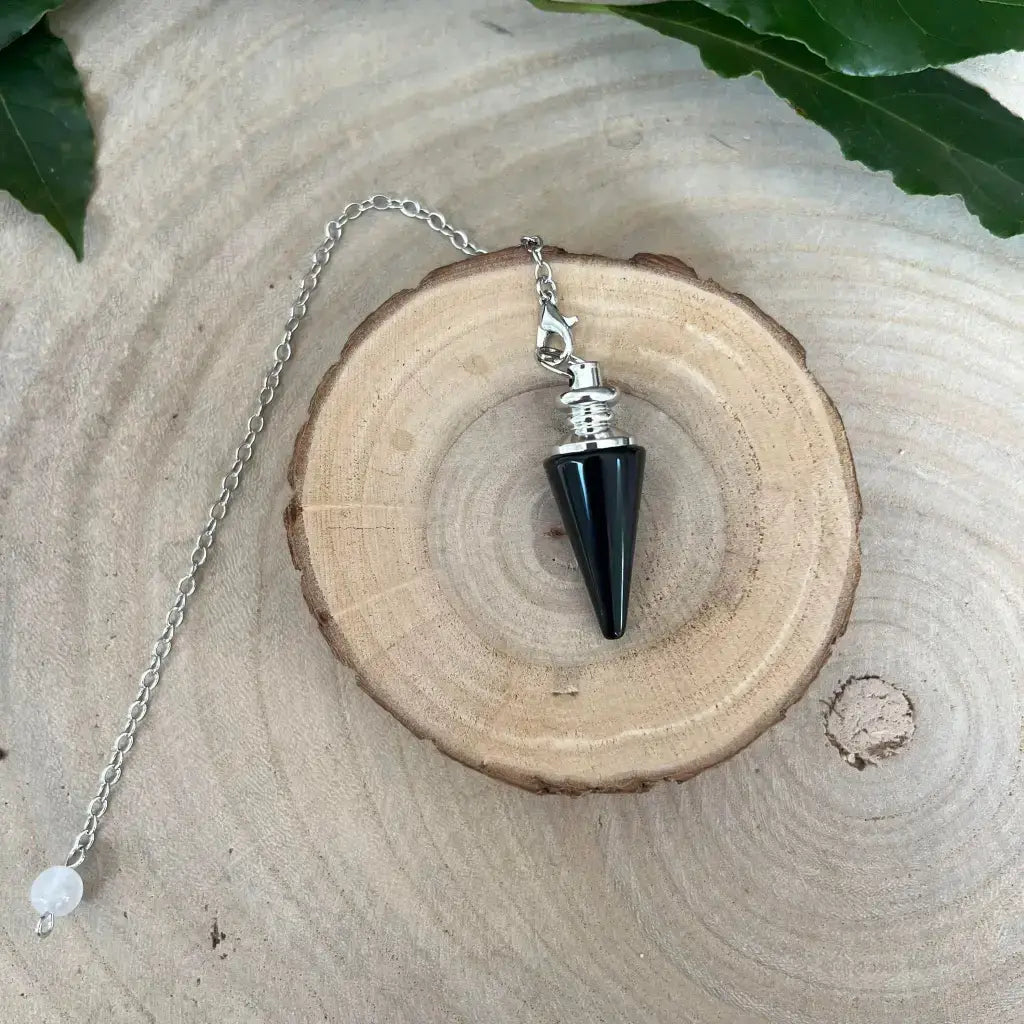 Pendule en Obsidienne Noire conique avec monture argentée et chaîne posé sur tranche de bois pour radiesthésie