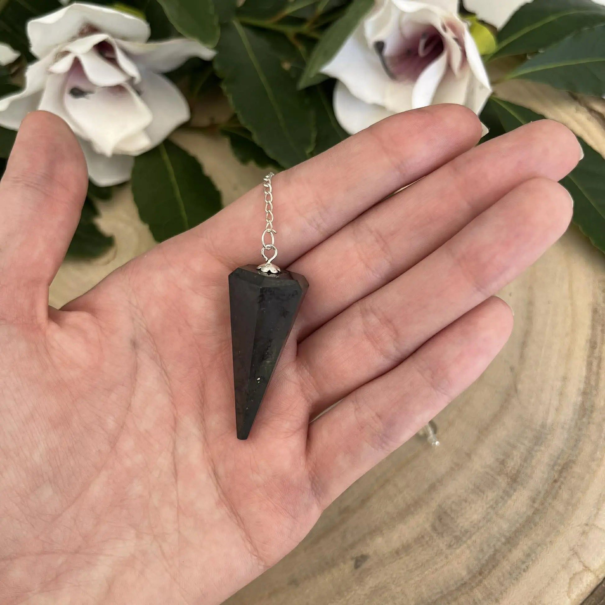 Pendule shungite en pierre naturelle noire avec chaîne argentée tenue dans une main pour protection et radiesthésie