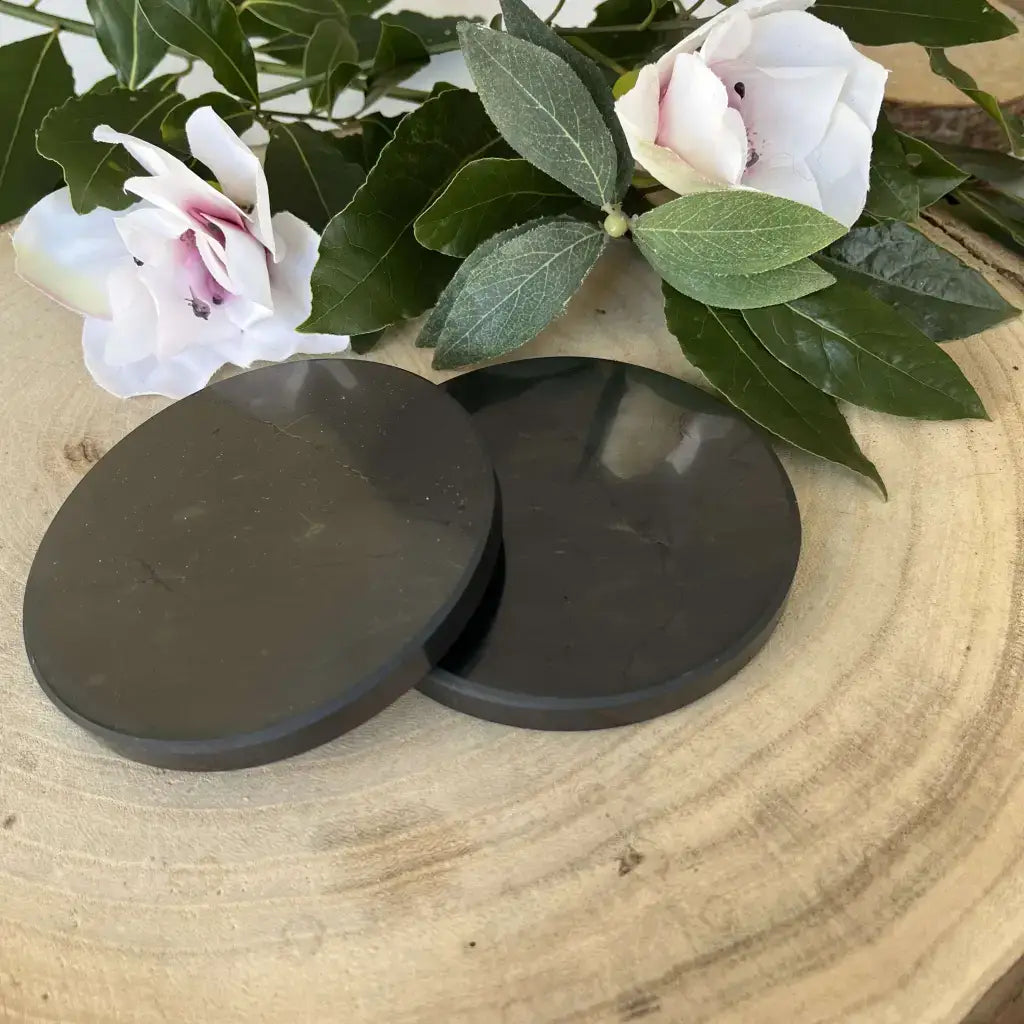 Plaque Shungite Protection Aura de Roche avec fleurs décoratives en arrière-plan sur une surface en bois